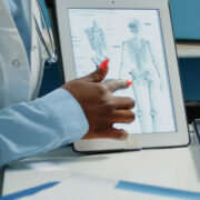 Close up of human skeleton image on tablet for osteopathy examination in doctors office. Doctor holding device with bones anatomy for osteoporosis diagnosis and healthcare treatment.