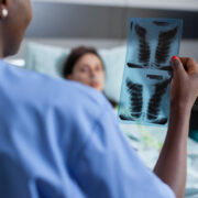 Close-up of afro american nurse analyzing lungs x-ray checking healdcare recovery. Sick woman patient resting in bed discussing disease treatment in hospital ward during therapy consultation