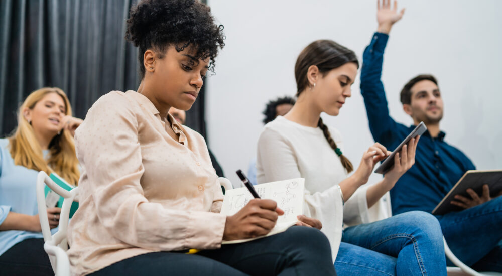 Group of young people sitting on conference together while raising their hands to ask a question. Business team meeting seminar training concept.